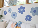 Felt Right wall art design in shades of blue in the shape of flowers on a white wall above a couch and below a window with a house plant in the corner.