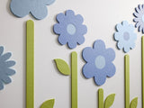 Felt Right wall art design of flowers with stems and grass in shades of blue on a white wall.