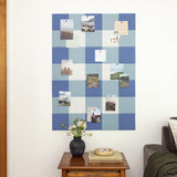 Blue checkered bulletin board with pinned photos on a white wall, next to a wooden side table with a vase and books.