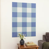 Checkered blue and white wall art above a wooden side table with a vase and books.