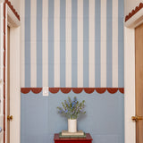 Decorative felt wall with blue and white striped tiles and a vase with flowers on a red table.