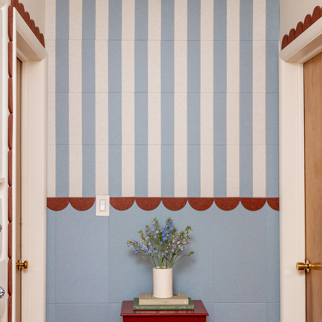 Decorative felt wall with blue and white striped tiles and a vase with flowers on a red table.