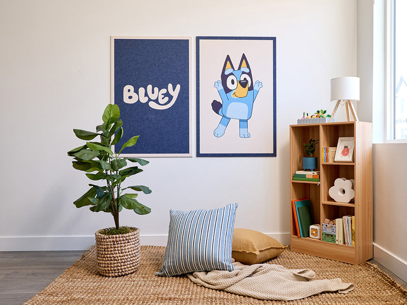 Room interior with 'Bluey' wall decor on the wall, a plant, and a bookshelf.