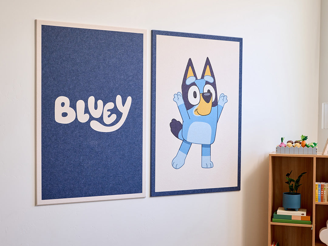 Two framed felt tiles on a wall, one with the word 'Bluey' and the other featuring a blue cartoon character.