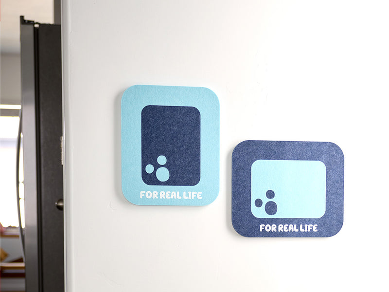 Two bluey themed felt tiles with a black circle and text 'FOR REAL LIFE' on a white wall.