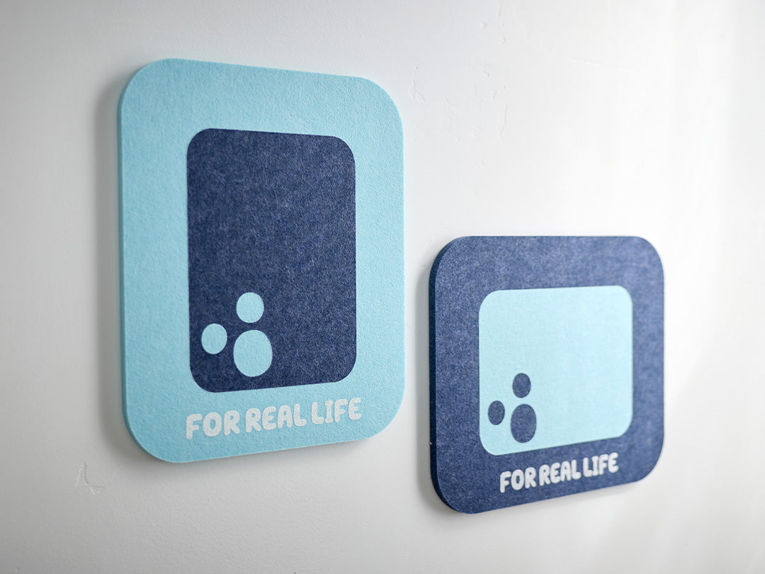 Two bluey themed felt tiles with a black circle and text 'FOR REAL LIFE' on a white wall.