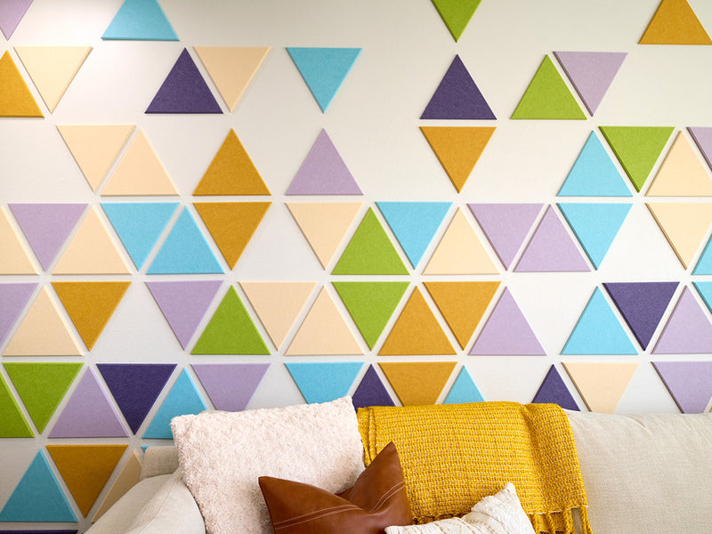 Colorful geometric triangle-patterned wall panels with a sofa and pillows below.