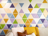 Felt Right wall art design using triangles in shades of yellow, green, blue, and purple on a white wall in a living room space behind a couch.