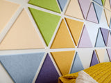 Felt Right wall art design using triangles in shades of yellow, green, blue, and purple on a white wall.