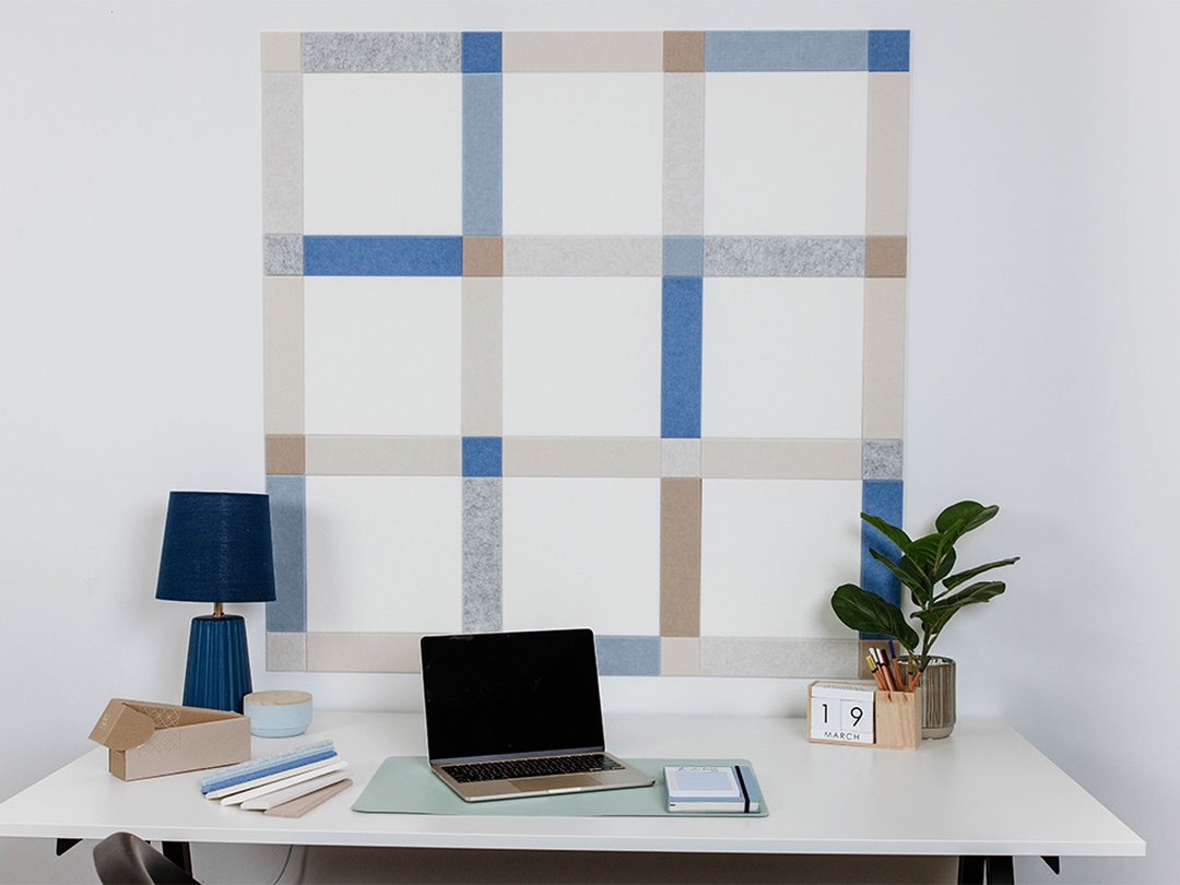 Felt Right wall art design using shades of blue, grey, and cream to created a plaid pattern on a white wall behind a desk with a laptop on it.