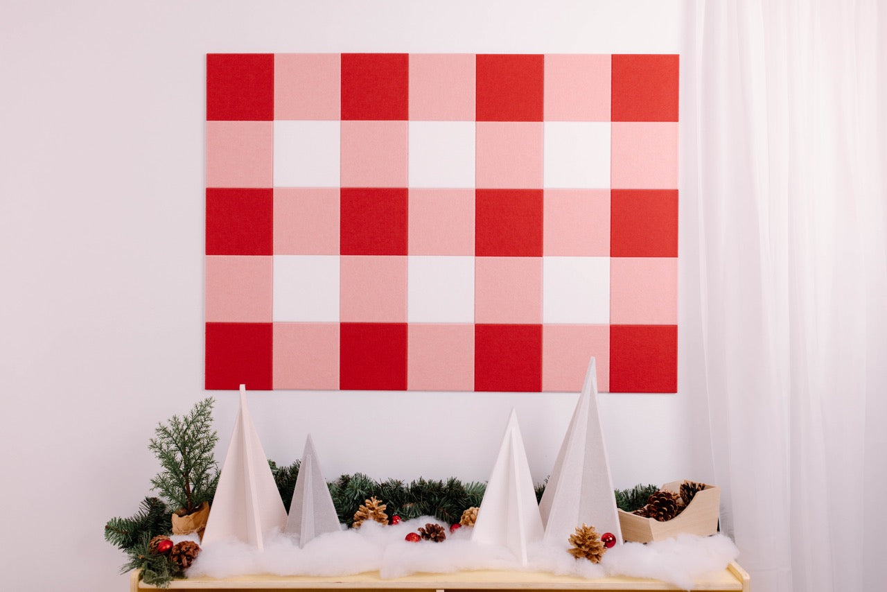 Decorative wall art with red and pink checkered pattern above a table with Christmas decorations.