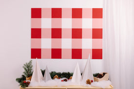 Decorative wall art with red and pink checkered pattern above a table with Christmas decorations.