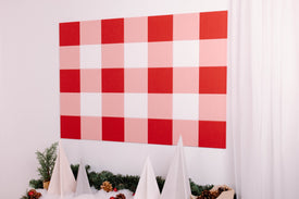 Red and pink checkered backdrop with white decorative elements and greenery.