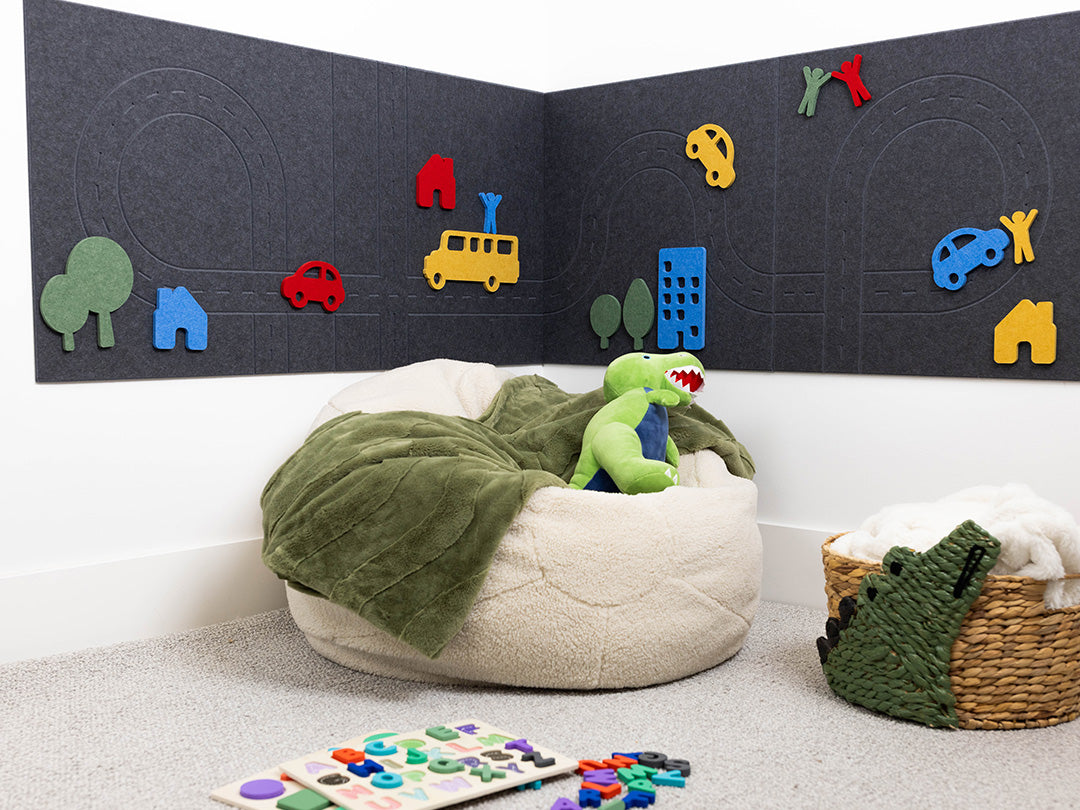 Children's play area with bean bag, toys, and felt cityscape on a wall.