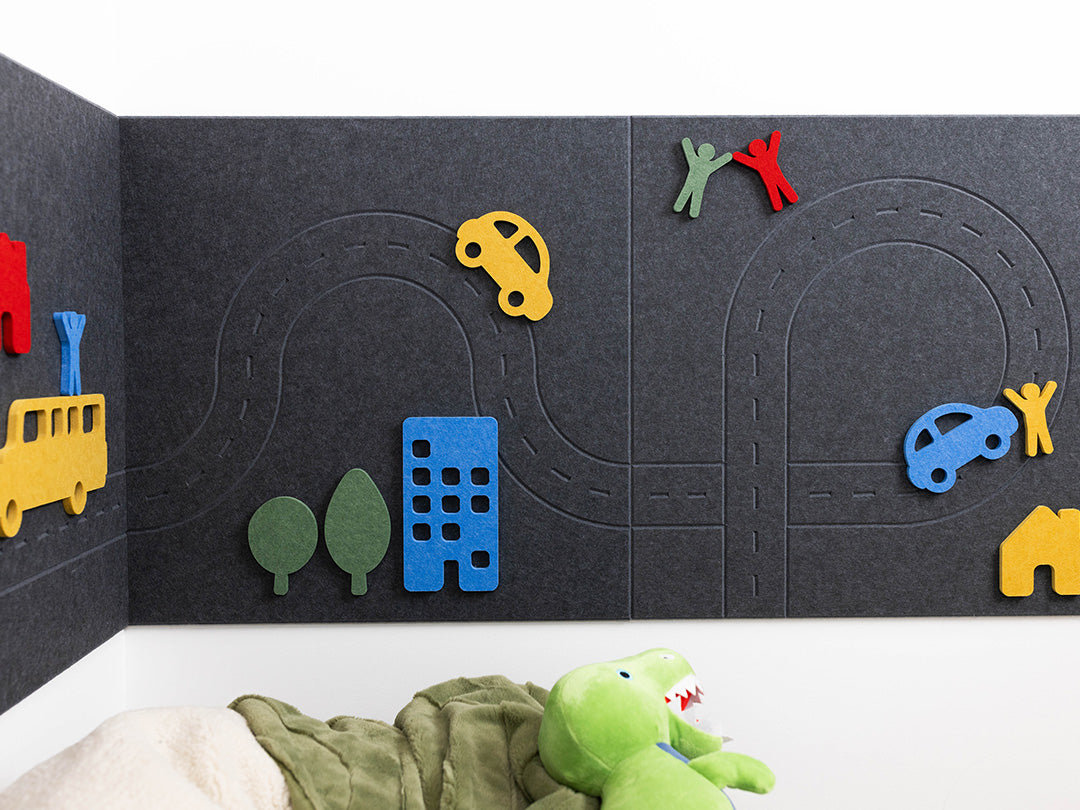 Children's play area with toy cars, buildings, and a plush toy on a black felt wall.