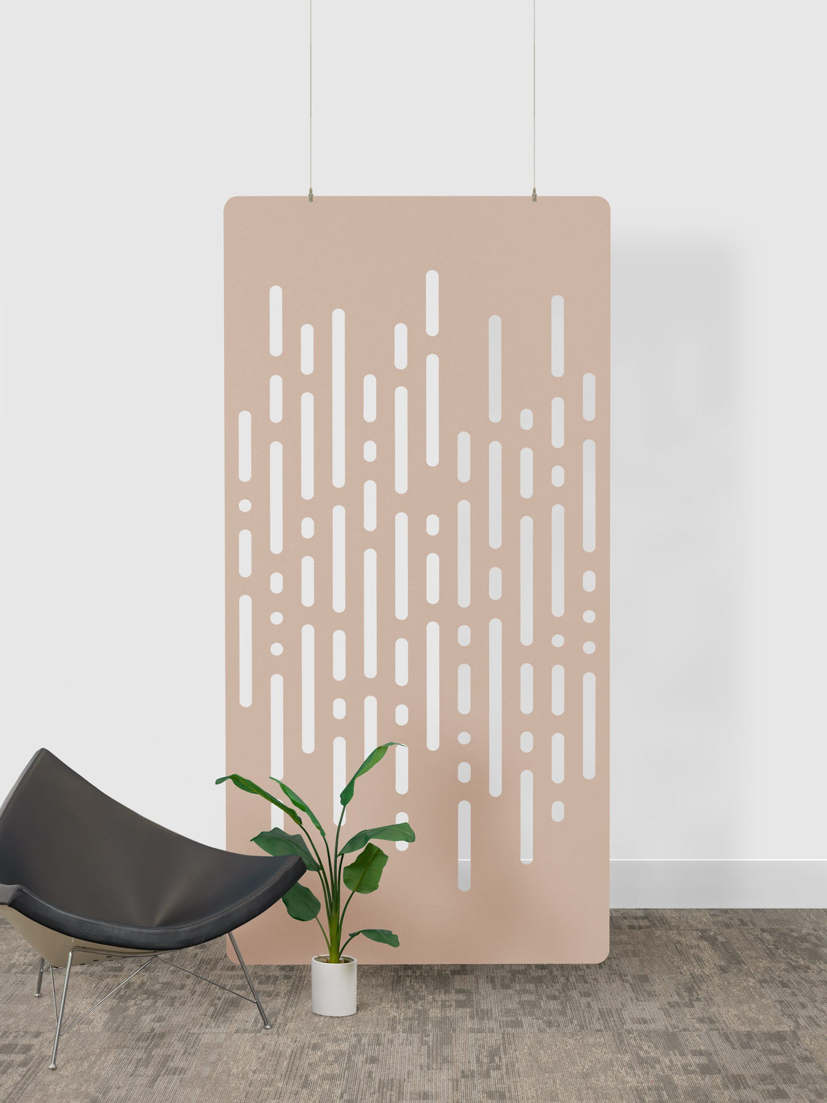 Beige perforated acoustic felt panel panel with white patterns against a white wall, with a black chair and plant in the foreground.