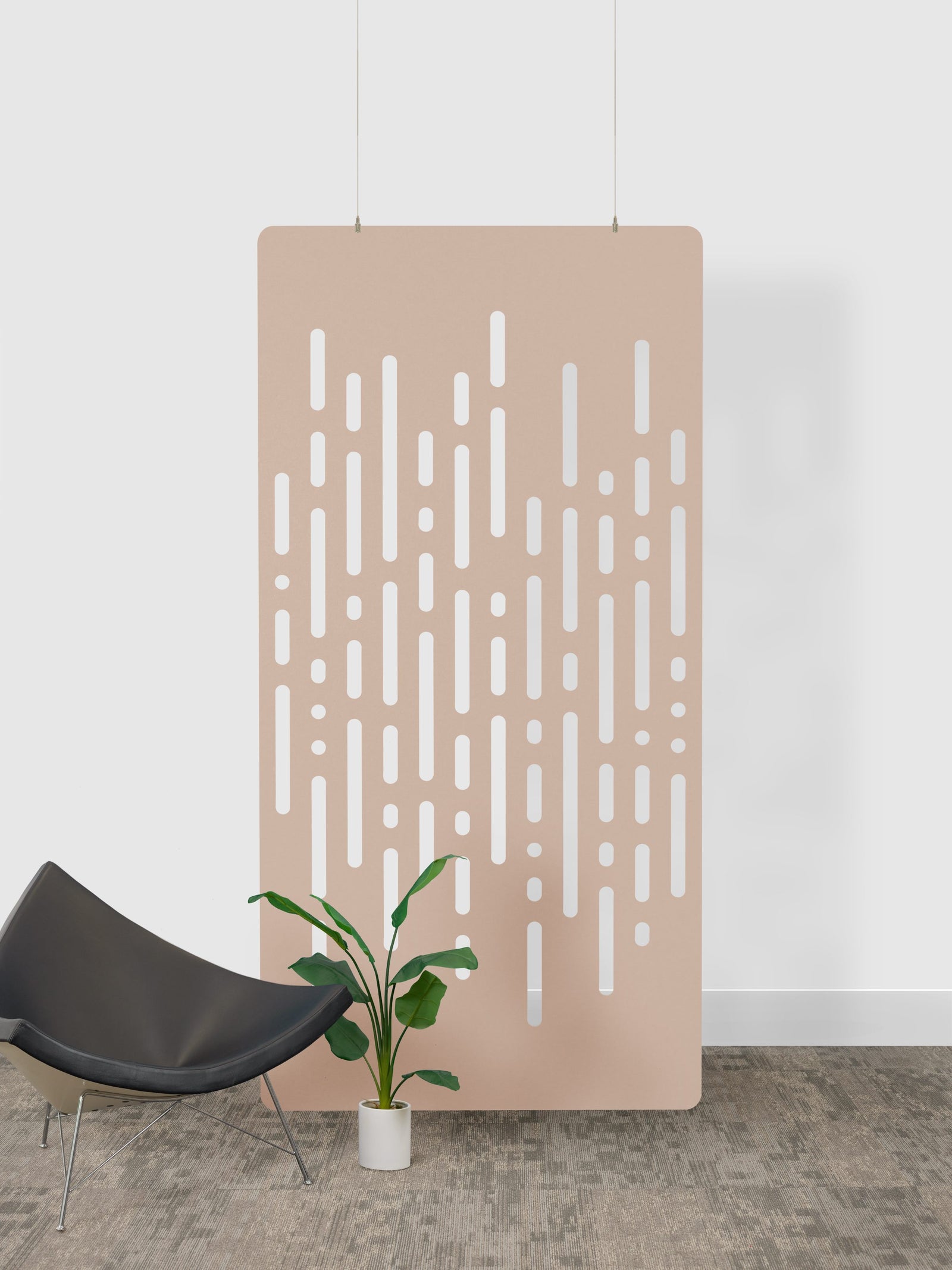 Beige perforated acoustic felt panel panel with white patterns against a white wall, with a black chair and plant in the foreground.