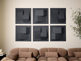 Six dark gray tiles with geometric 3D shapes in varying shades arranged in a 2x3 grid on a beige wall above a tan sofa.