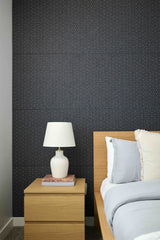 Bedroom with dark patterned wallpaper, wooden nightstand, and bed with pillows.