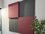 Four fabric-covered acoustic panels in burgundy and charcoal gray arranged in a 3D staggered pattern on a white wall.
