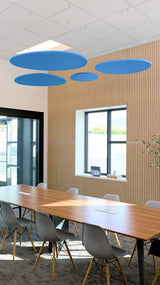 Four blue elliptical acoustic baffles suspended from ceiling in modern office space above wooden conference table.