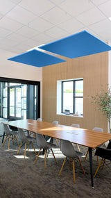 Two blue square acoustic panels suspended from ceiling above conference table in office space.