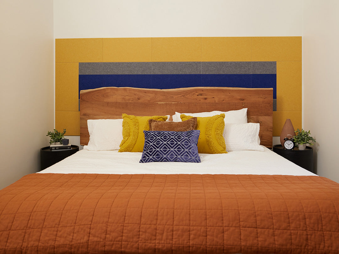 A Felt Right wall design in blue yellow and grey felt tiles on a white wall in a bedroom behind a bed 
