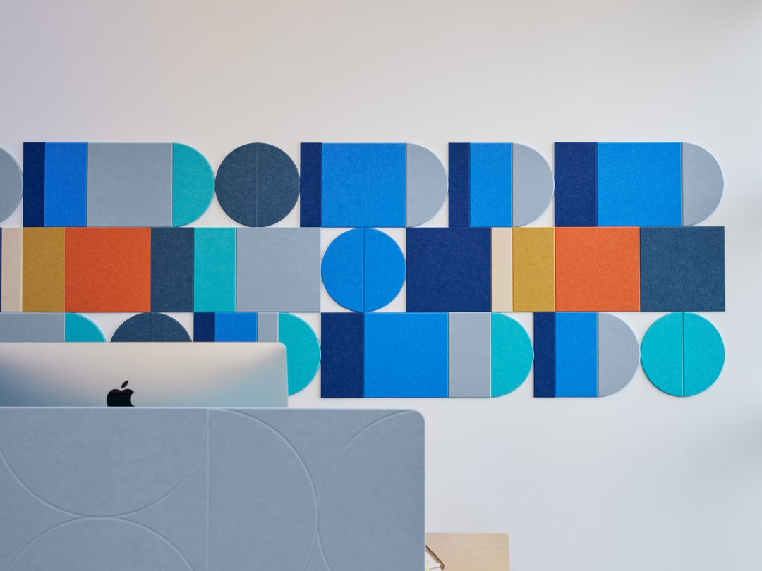 Felt Right wall art design using shades of blue and orange to create a geometric design on a white wall behind a desk with a computer on it.