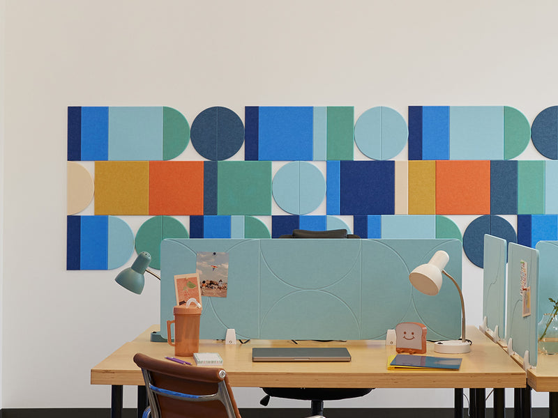 A Felt Right wall art design in shades of blue, orange, and yellow creating a geometric wall art pattern behind a desk 
