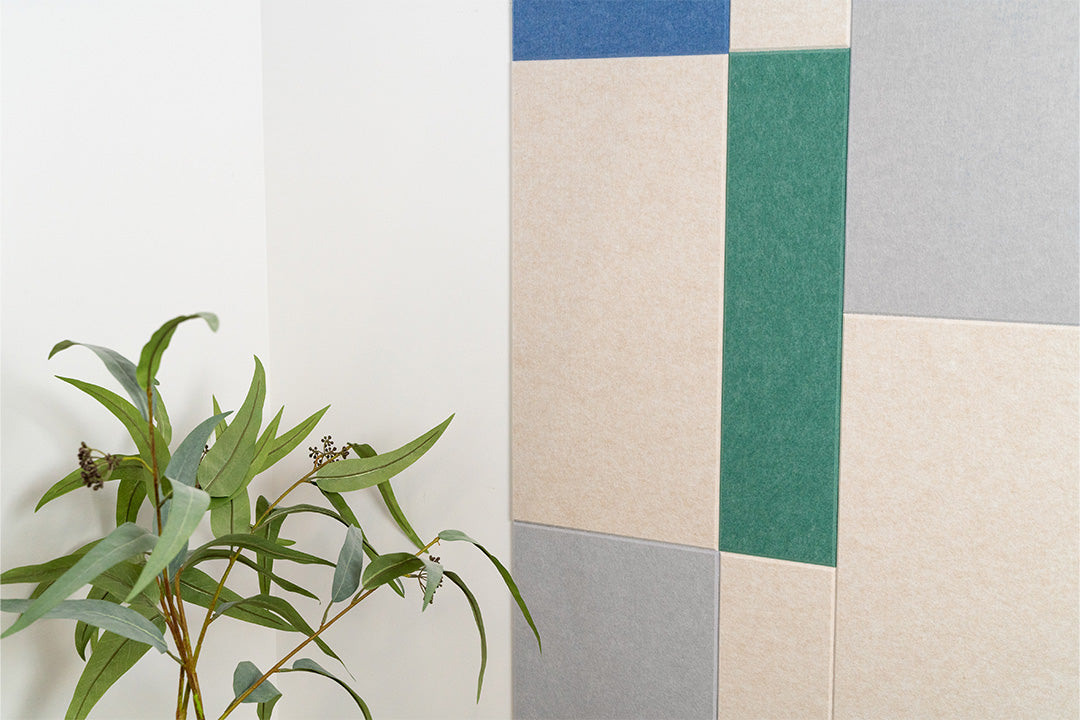 A Felt Right wall art design in shades of cream, blues, and green next to a plant.