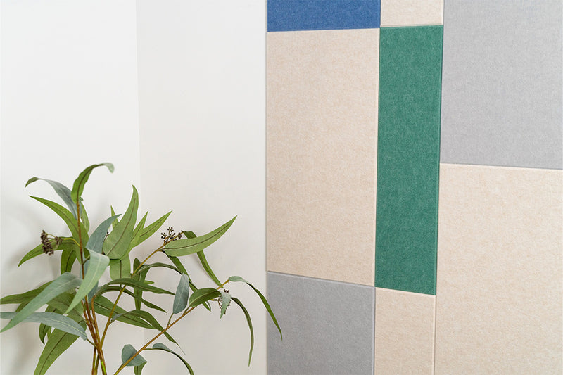 A Felt Right wall art design in shades of cream, blues, and green next to a plant.