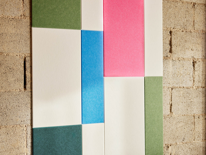 Color swatch tiles in green, pink, blue, and beige on a textured wall.