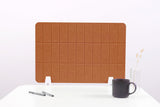 Brown leather grid desk divider with white base supports, displayed on white desk with office accessories.