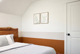 Bedroom wall with lower wainscoting in warm wood tone and upper section in white, paired with wooden bed frame.