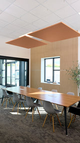 Two tan square acoustic ceiling baffles suspended above a conference table in an office space.