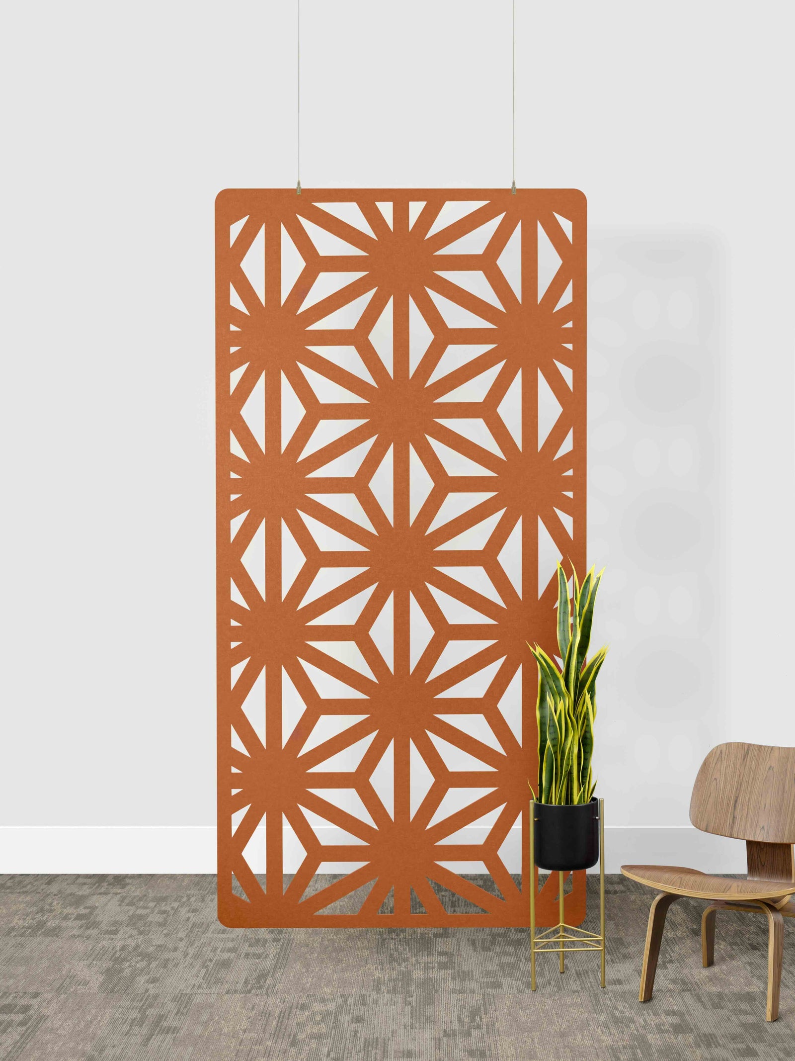Decorative orange panel with geometric pattern in a room setting with a chair and plant.