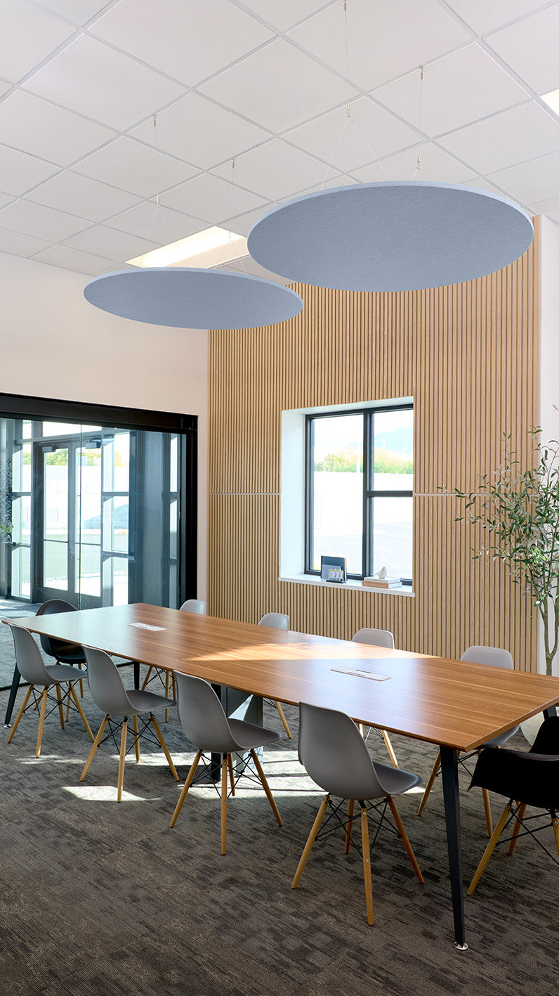 Two blue-gray circular flat baffles suspended from ceiling above a conference table in an office space.