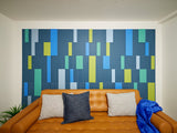 Abstract wall art with layered rectangular blocks in blue, green, yellow, and white tones on dark blue background.
