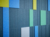 Stacked rectangular panels in blue, green, yellow, gray, and white with vertical ribbed texture throughout.