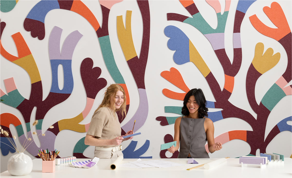 Two women standing in front of a colorful abstract wall mural.