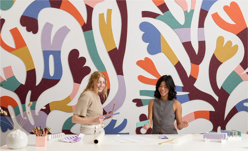 Two women standing in front of a colorful abstract wall mural.
