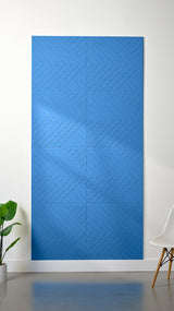 Light blue Felt Right 4’ x 8’ PET felt panel with geometric lines engraved into the material against a white wall. A plant and chair are in the foreground.