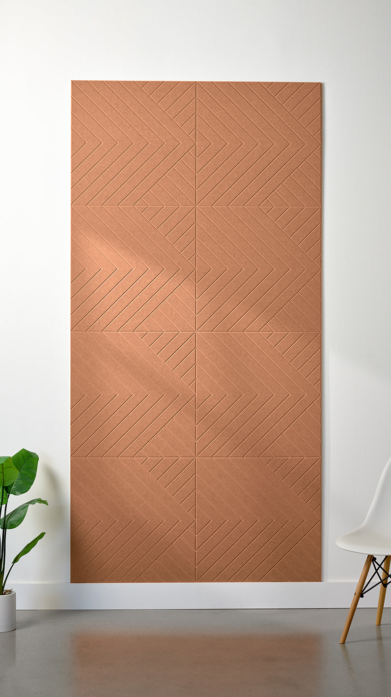 Light orange Felt Right 4’ x 8’ PET felt panel with geometric lines engraved into the material against a white wall. A plant and chair are in the foreground.
