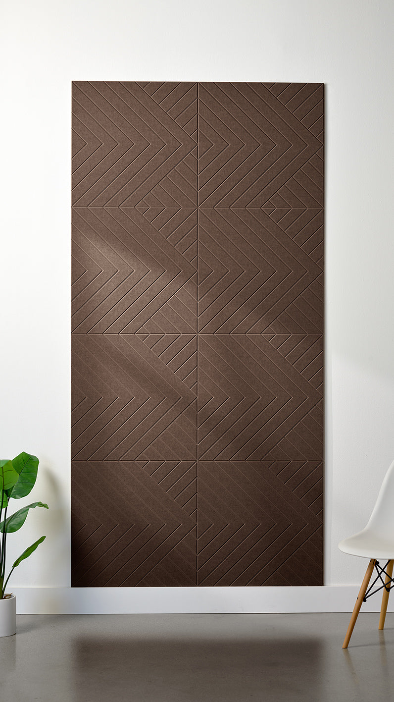 Brown Felt Right 4’ x 8’ PET felt panel with geometric lines engraved into the material against a white wall. A plant and chair are in the foreground.