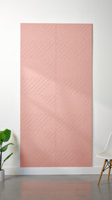Light pink Felt Right 4’ x 8’ PET felt panel with geometric lines engraved into the material against a white wall. A plant and chair are in the foreground.