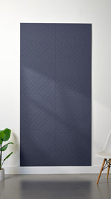Indigo Felt Right 4’ x 8’ PET felt panel with geometric lines engraved into the material against a white wall. A plant and chair are in the foreground.