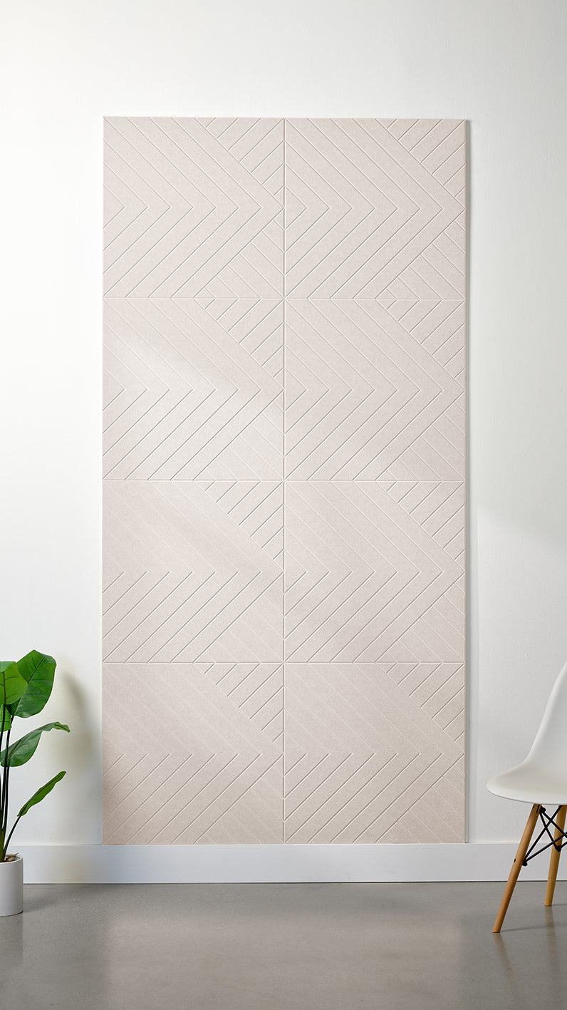 Heathered beige Felt Right 4’ x 8’ PET felt panel with geometric lines engraved into the material against a white wall. A plant and chair are in the foreground.