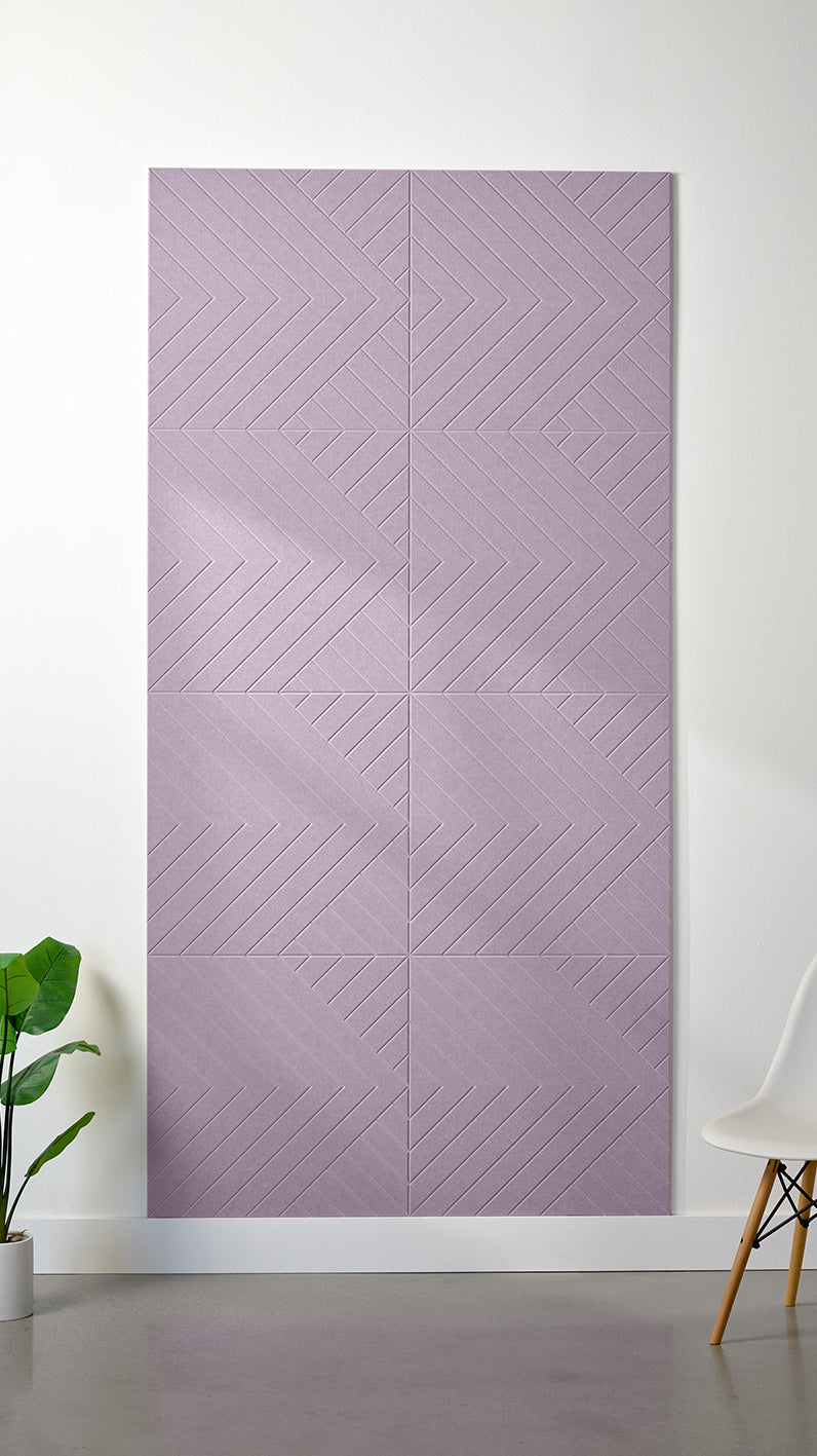 Light purple Felt Right 4’ x 8’ PET felt panel with geometric lines engraved into the material against a white wall. A plant and chair are in the foreground.