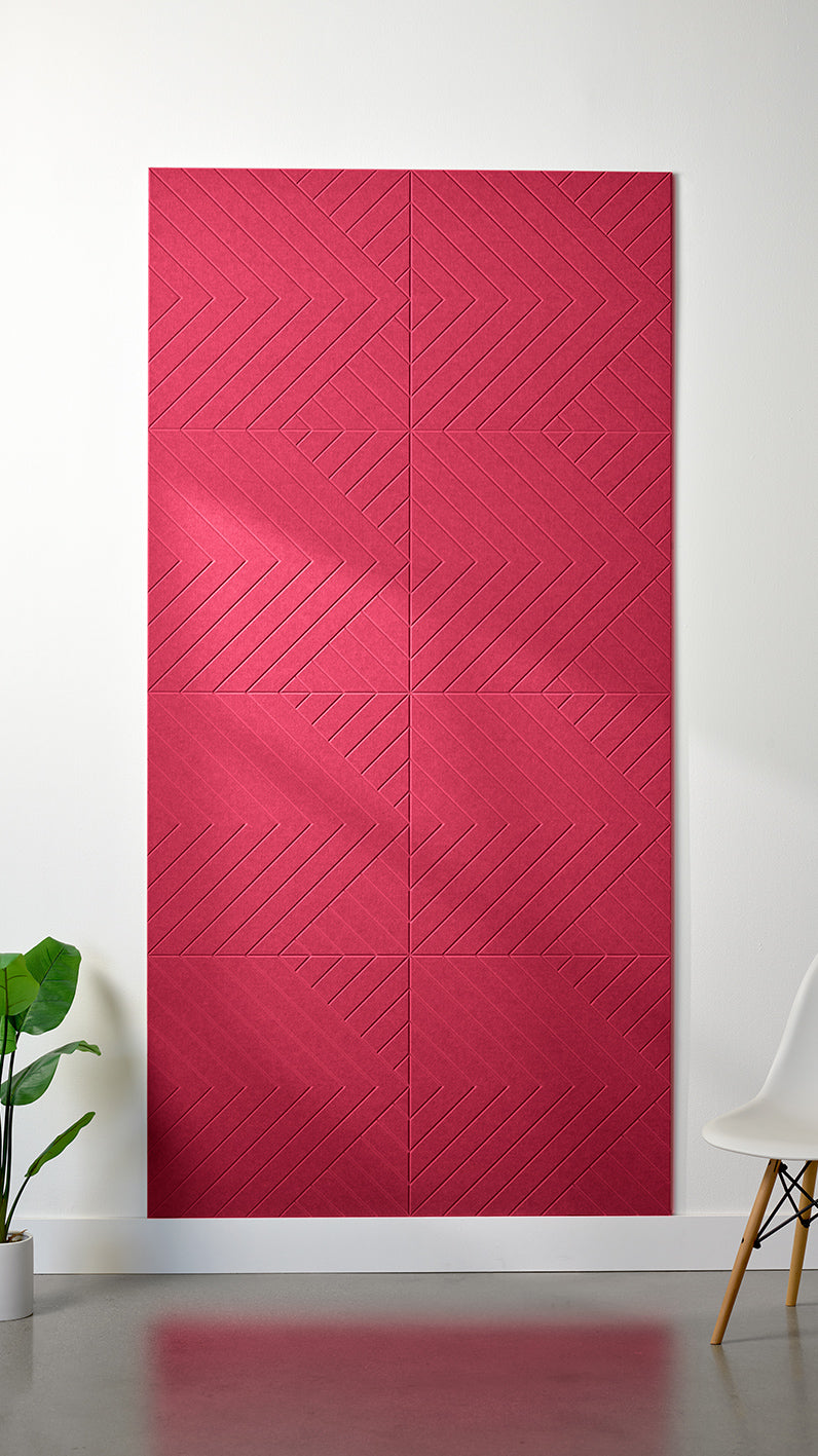 Bright red Felt Right 4’ x 8’ PET felt panel with geometric lines engraved into the material against a white wall. A plant and chair are in the foreground.