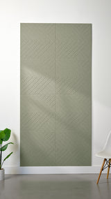 Sage green Felt Right 4’ x 8’ PET felt panel with geometric lines engraved into the material against a white wall. A plant and chair are in the foreground.